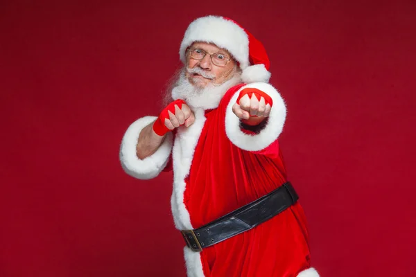 Jul. Jultomte med röda bandage sår på händerna för boxning imiterar sparkar. Kickboxning, karate, boxning. Isolerad på röd bakgrund. — Stockfoto