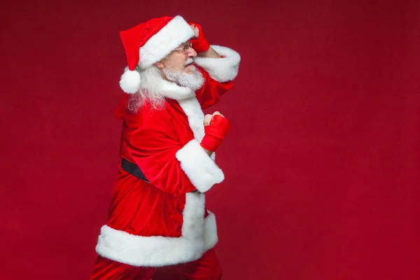 Weihnachten. Weihnachtsmann mit roten Bandagen, die sich um seine Hände wickeln, um Tritte zu imitieren. Kickboxen, Karate, Boxen. isoliert auf rotem Hintergrund. — Stockfoto