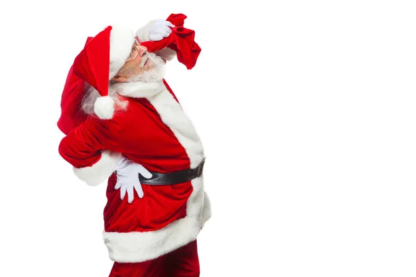 Navidad. Santa Claus está sufriendo de dolor de espalda y sostiene una bolsa roja con regalos en la espalda. Aislado sobre fondo blanco . —  Fotos de Stock