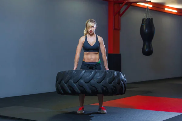 Apto atleta feminino exercitar-se com um pneu enorme, girando e transportar no ginásio. Crossfit mulher exercitando com pneu grande — Fotografia de Stock