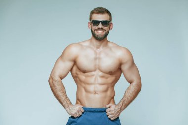 .vücut geliştirmeci poz. Güzel sportif adam erkek güç. Fitness mavi şort ve güneş gözlüğü kaslı. izole gri arka plan üzerinde. Kas gövde olan adam. Güçlü atletik erkek Fitness modeli gövde