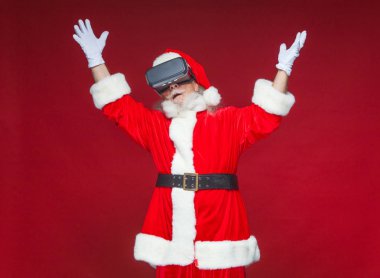 Noel. Noel Baba siyah sanal gerçeklik bardaklarda elleriyle hareketleri yapar. Sürpriz, duygu. Yeni teknoloji. Kırmızı zemin üzerine izole.