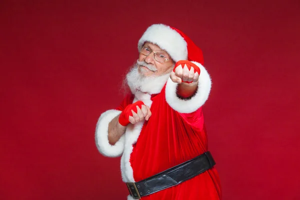 Weihnachten. Weihnachtsmann mit roten Bandagen, die sich um seine Hände wickeln, um Tritte zu imitieren. Kickboxen, Karate, Boxen. isoliert auf rotem Hintergrund. — Stockfoto