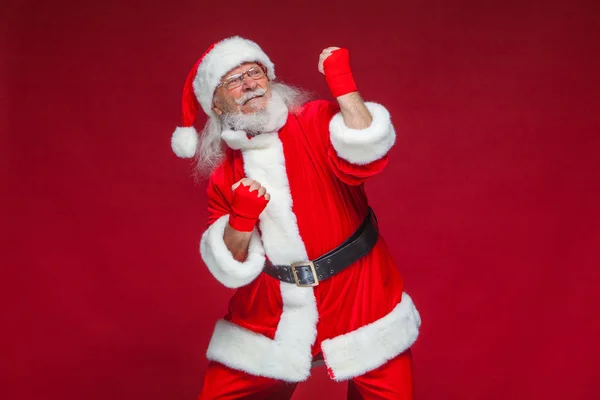 Navidad. Santa Claus con vendajes rojos en las manos para el boxeo imita patadas. Kickboxing, karate, boxeo. Aislado sobre fondo rojo . —  Fotos de Stock