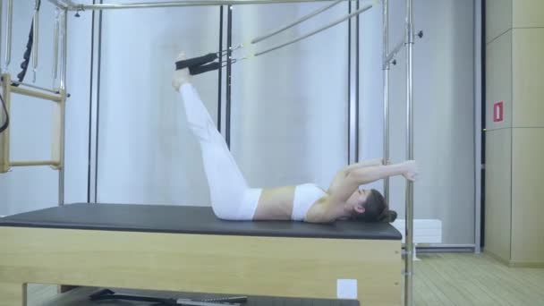 Женщина в белой одежде практикует упражнения на растяжку на реформаторе в спортзале. все серии под номером 01234567890001 . — стоковое видео