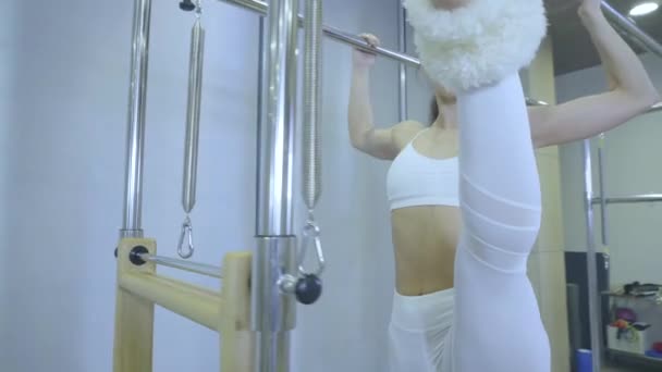 Пилатес. Женщина в белой одежде практикует упражнения на растяжку на реформаторе в спортзале. все серии под номером 01234567890001 . — стоковое видео