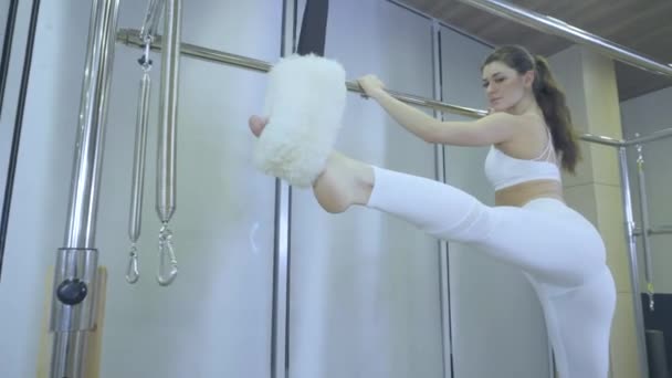 Pilates. Frau in weißen Kleidern beim Dehnübungen am Reformer im Fitnessstudio. alle Serien nach Nummer 01234567890001. — Stockvideo