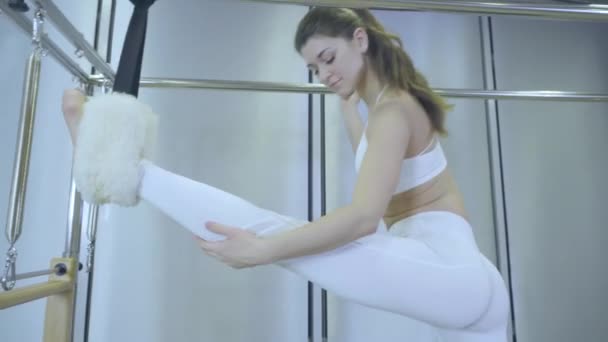 Pilates. Frau in weißen Kleidern beim Dehnübungen am Reformer im Fitnessstudio. alle Serien nach Nummer 01234567890001. — Stockvideo