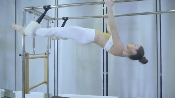 Cvičení Pilates. Žena v bílých šatech cvičí protahovací cvičení na reformátora v tělocvičně. všechny série podle čísla 01234567890001. — Stock video