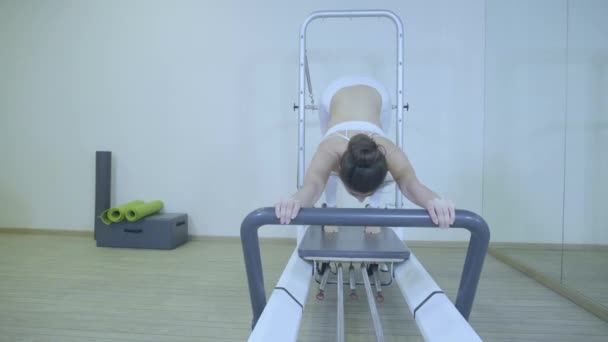 Pilates. Mujer con ropa blanca practicando ejercicio de estiramiento en reformador en gimnasio. todas las series por número 01234567890001 . — Vídeo de stock