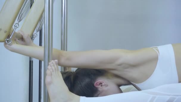 Cvičení Pilates. Žena v bílých šatech cvičí protahovací cvičení na reformátora v tělocvičně. všechny série podle čísla 01234567890001. — Stock video