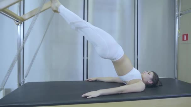 Pilates. Woman in white clothes practicing stretching exercise on reformer in gym. all series by number 01234567890001. — Stock Video