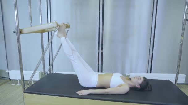 Pilates. Kvinna i vita kläder öva stretching övning på reformator i gymmet. Alla serier av nummer 01234567890001. — Stockvideo