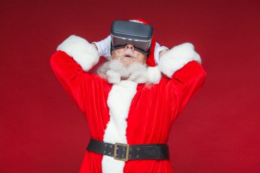 Noel. Noel Baba siyah sanal gerçeklik bardaklarda elleriyle hareketleri yapar. Sürpriz, duygu. Yeni teknoloji. Kırmızı zemin üzerine izole.