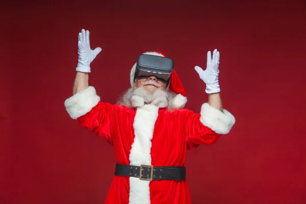 Noël. Père Noël en noir lunettes de réalité virtuelle fait des gestes avec ses mains. Surprise, émotion. Nouvelle technologie. Isolé sur fond rouge . — Photo