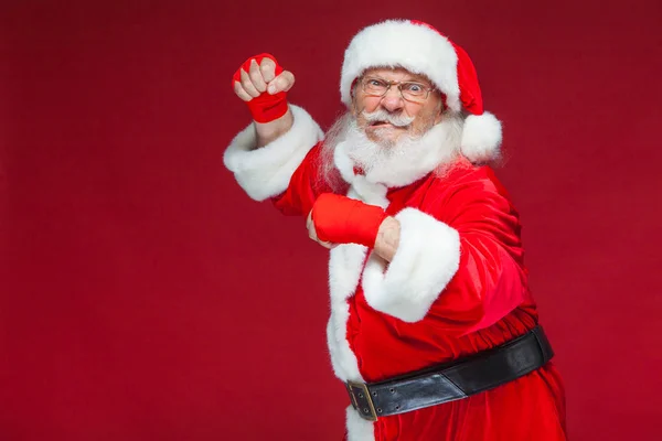 Weihnachten. Weihnachtsmann mit roten Bandagen, die sich um seine Hände wickeln, um Tritte zu imitieren. Kickboxen, Karate, Boxen. isoliert auf rotem Hintergrund. — Stockfoto