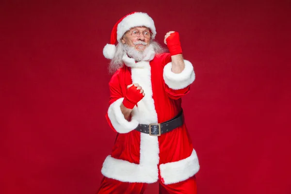 Jul. Jultomte med röda bandage sår på händerna för boxning imiterar sparkar. Kickboxning, karate, boxning. Isolerad på röd bakgrund. — Stockfoto