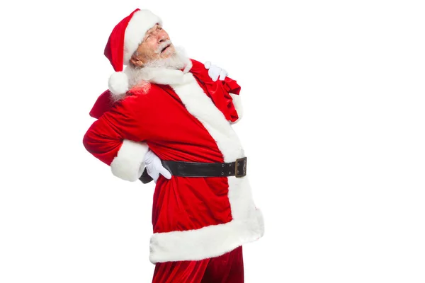 Jul. Santa Claus lider av ryggvärk och innehar en röd väska med gåvor på ryggen. Isolerad på vit bakgrund. — Stockfoto