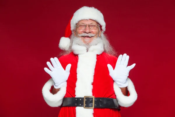 Christmas. Good Santa Claus in white gloves shows faces, grimaces, shows his tongue. Not standard behavior. Isolated on red background. — Stock Photo, Image