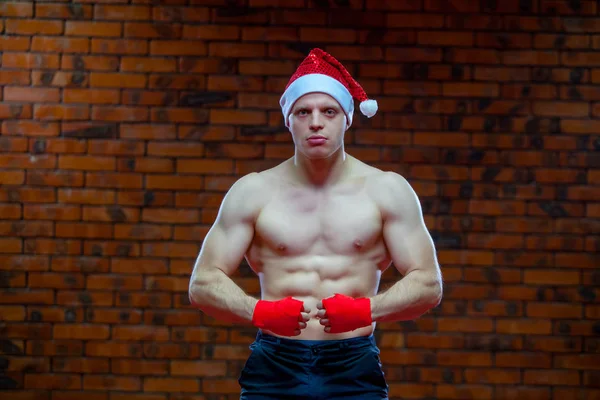 Noel. Noel Baba kırmızı boks kaslı savaşçı kickbox bir tuğla duvar arka sargılar. — Stok fotoğraf