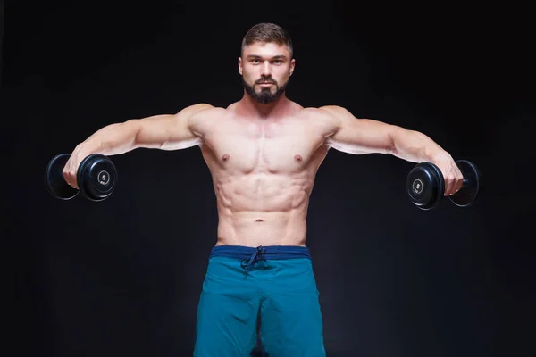 Muscular bodybuilder guy doing exercises with dumbbell over black background — Stock Photo, Image
