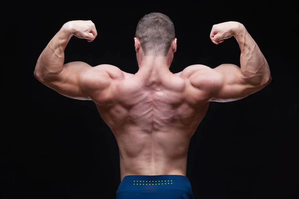 Rear view of healthy muscular young man with arms bent out isolated on black background — Stock Photo, Image