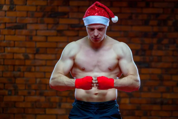 Noel. Noel Baba kırmızı boks kaslı savaşçı kickbox bir tuğla duvar arka sargılar. — Stok fotoğraf