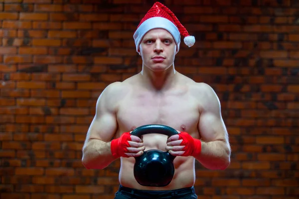 Noel. Noel Baba kırmızı boks kaslı savaşçı kickbox bir tuğla duvar arka sargı bezi. Spor malzemeleri elinde tutar — Stok fotoğraf