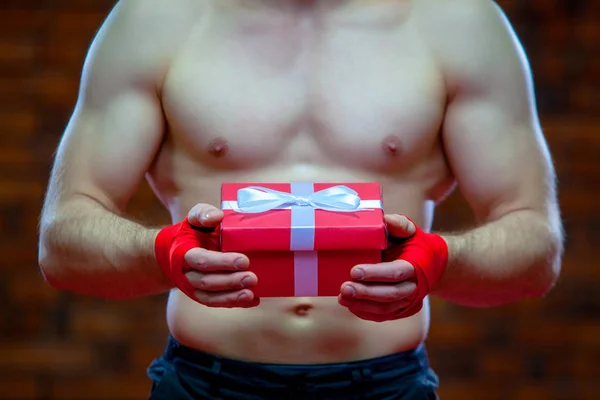 Navidad. Muscular Fighter kickbox boxeo Santa Claus Con vendajes rojos el fondo de una pared de ladrillo. Lleva una caja de regalo roja —  Fotos de Stock