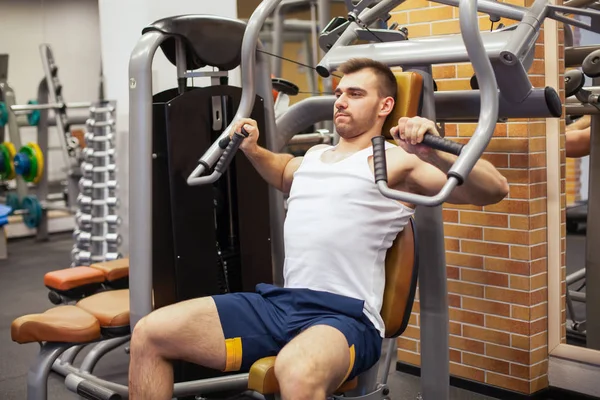 Hombre haciendo ejercicio en el gimnasio. Atleta de fitness haciendo ejercicios de pecho en la máquina de press de banca vertical —  Fotos de Stock