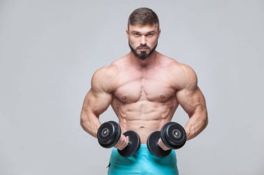 Gri arka plan üzerinde halter alıştırmalar yapan kaslı vücut geliştirmeci adam