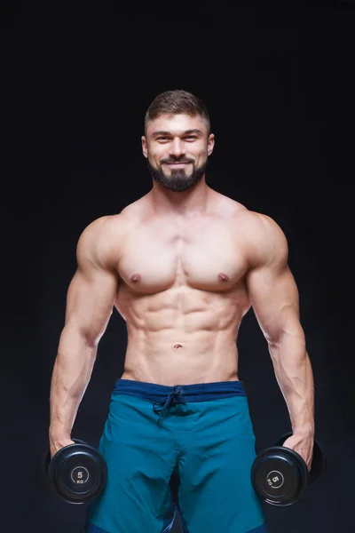 Glimlach. Gespierde bodybuilder man doen oefeningen met dumbbell op zwarte achtergrond — Stockfoto