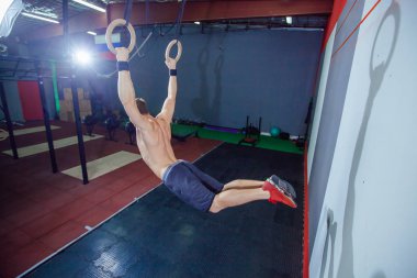 Jimnastik halkaları üzerinde spor salonunda egzersiz kas-up egzersiz yoğun yapan genç erkek çapraz yerleştirmek.