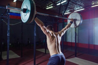 Arkadan bir yakışıklı sporcu portresi. Atlet halter başının üzerine yükseltir. Stüdyo çekim koyu tonda. Çapraz tarzı uygun, deadlift