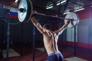 Arkadan bir yakışıklı sporcu portresi. Atlet halter başının üzerine yükseltir. Stüdyo çekim koyu tonda. Çapraz tarzı uygun, deadlift