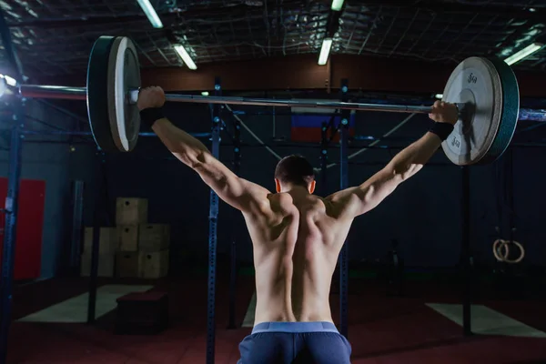 Portrait of a handsome athlete from behind. Athlete raises the barbell over your head. Studio shots in the dark tone. Cross style fit, deadlift — Stock Photo, Image