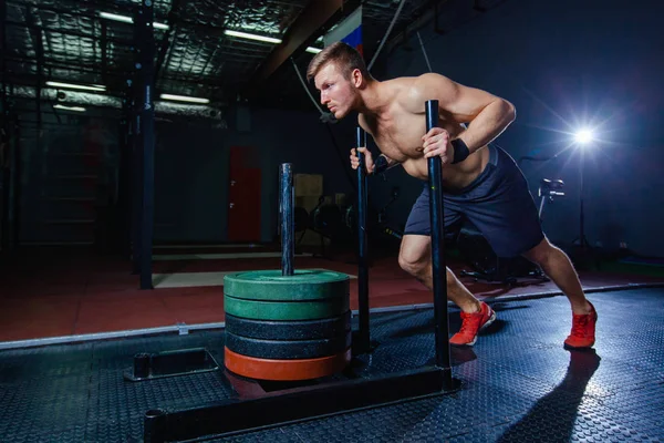 Trineo empuje hombre empujando pesas ejercicio de entrenamiento en el gimnasio. Ajuste estilo cruz — Foto de Stock