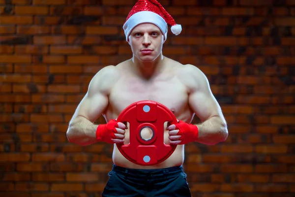 Christmas. Muscular Fighter kickbox boxing Santa Claus With Red Bandages the background of a brick wall. Holds sports equipment in his hands — Stock Photo, Image