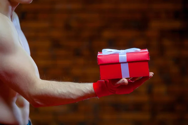 クリスマス。赤いサンタ クロースをボクシング筋肉の戦闘機 kickbox 包帯レンガの壁の背景です。赤いギフト ボックスを保持します。 — ストック写真
