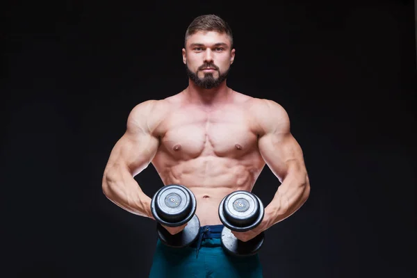 Muscular bodybuilder guy doing exercises with dumbbell over black background — Stock Photo, Image