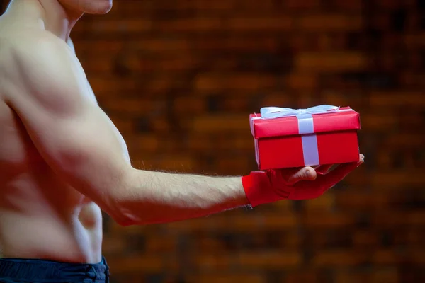 Navidad. Muscular Fighter kickbox boxeo Santa Claus Con vendajes rojos el fondo de una pared de ladrillo. Lleva una caja de regalo roja —  Fotos de Stock