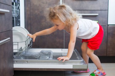 sevimli sarışın bebek kız mutfakta tabak bulaşık yıkama makinesi dışına alarak yardım
