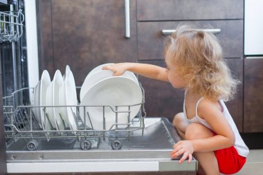 sevimli sarışın bebek kız mutfakta tabak bulaşık yıkama makinesi dışına alarak yardım