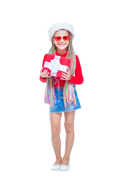 Una chica con sombrero de Santas. Retrato de una niña linda sosteniendo la caja del regalo de Navidad, niña pequeña abrazar su regalo con expresión feliz y divertida aislada en el fondo blanco. Regalo de vacaciones — Foto de Stock