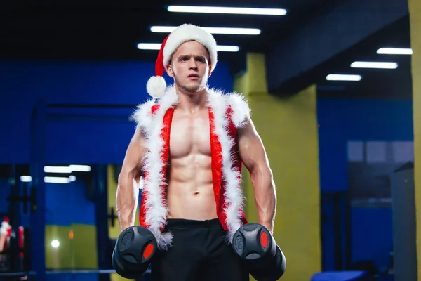 Svátky a oslavy, Silvestr, Vánoce, sport, kulturistika, zdravého životního stylu - svalová hezký sexy Santa Clause. Svalnatý kulturista chlap dělá cvičení s činkami nad v tělocvičně — Stock fotografie