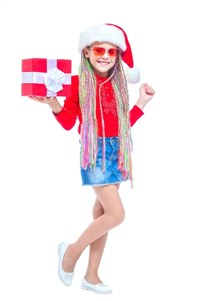 Una chica con sombrero de Santas. Retrato de una niña linda sosteniendo la caja del regalo de Navidad, niña pequeña abrazar su regalo con expresión feliz y divertida aislada en el fondo blanco. Regalo de vacaciones — Foto de Stock