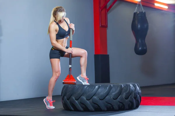 Fitness woman hitting wheel tire with hammer sledge in the gym.