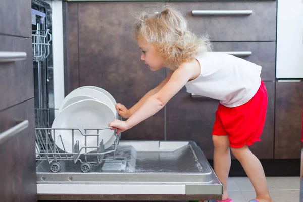Sevimli sarışın bebek kız mutfakta tabak bulaşık yıkama makinesi dışına alarak yardım — Stok fotoğraf