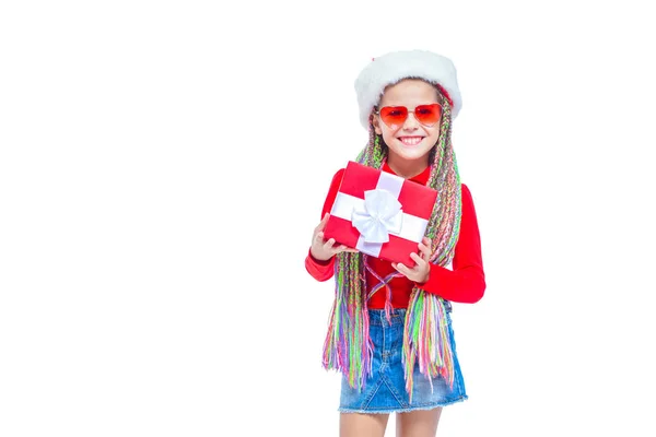 Una chica con sombrero de Santas. Retrato de una niña linda sosteniendo la caja del regalo de Navidad, niña pequeña abrazar su regalo con expresión feliz y divertida aislada en el fondo blanco. Regalo de vacaciones — Foto de Stock