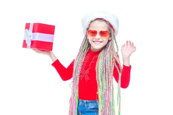 Una chica con sombrero de Santas. Retrato de una niña linda sosteniendo la caja del regalo de Navidad, niña pequeña abrazar su regalo con expresión feliz y divertida aislada en el fondo blanco. Regalo de vacaciones — Foto de Stock